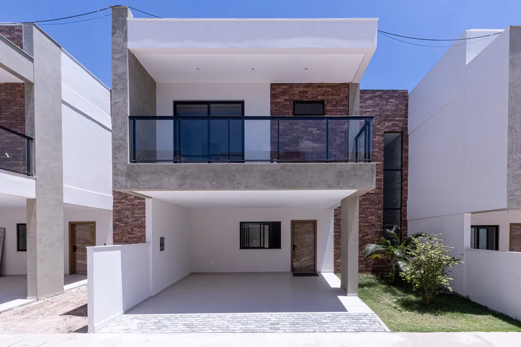 Foto frontal de uma casa do Tree Residence, com varanda de vidro na suíte master e garagem para dois carros