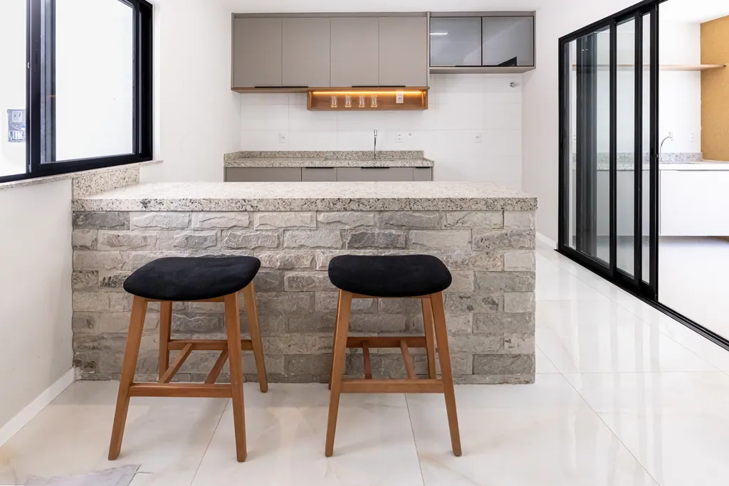 Cozinha da casa decorada com ilha revestida em pedra, bancada de granito e banquetas de madeira