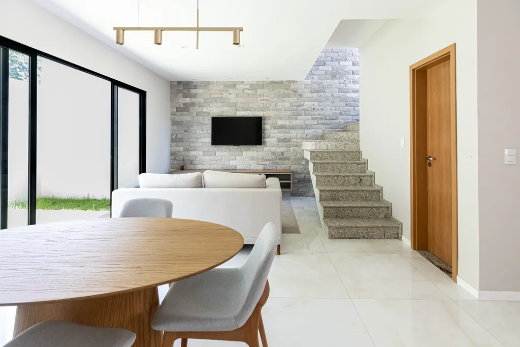 Sala de estar e jantar integradas da casa decorada, com parede de pedra, escada e porta de vidro para o quintal
