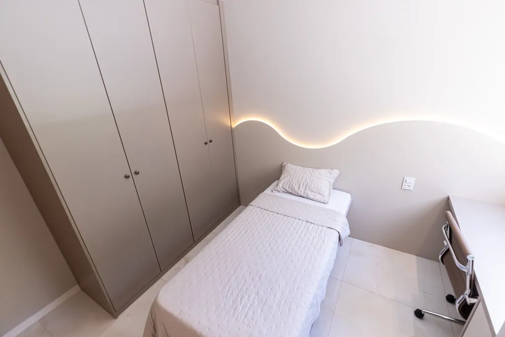 Suíte com iluminação indireta em curva na parede, armário planejado e bancada de estudos